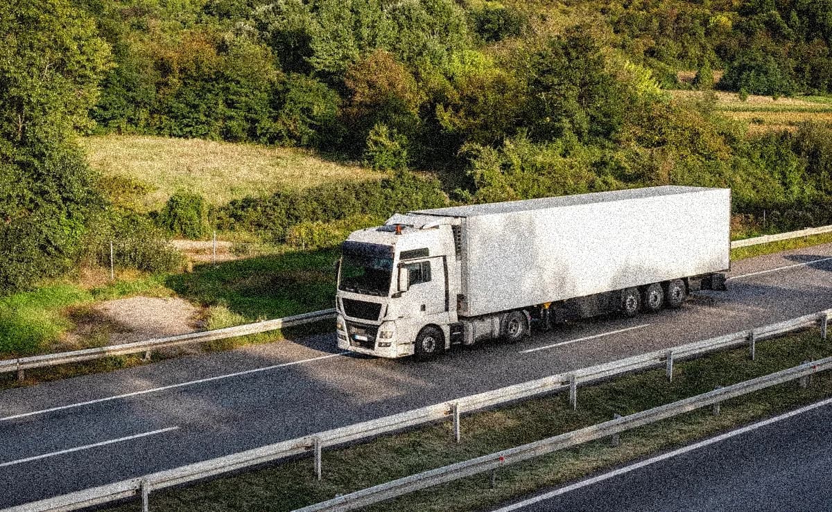 A white truck driving on a highway with forest in the background