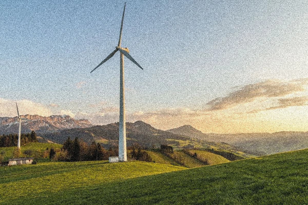 Two wind turbines in a hilly, desolate landscape with mountains in the background.